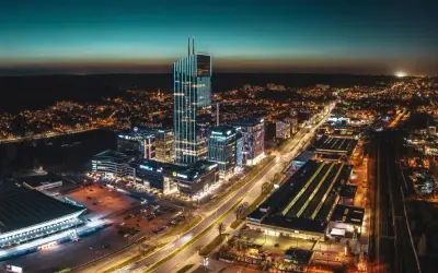 Widok z lotu ptaka na nowoczesne centrum miasta nocą, z oświetlonymi wieżowcami i ulicami.