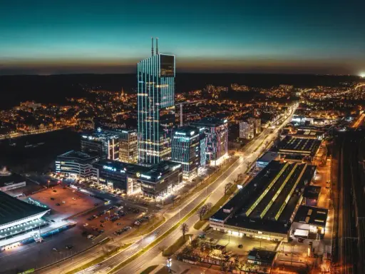 Widok z lotu ptaka na nowoczesne centrum miasta nocą, z oświetlonymi wieżowcami i ulicami.