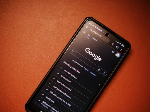 Smartfon z włączoną wyszukiwarką Google i listą popularnych wyszukiwań.